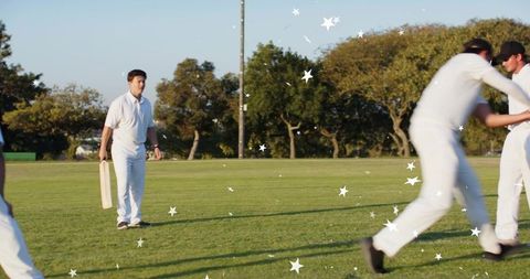 Standing batsman holding bat while teammates celebrating on sunny cricket field