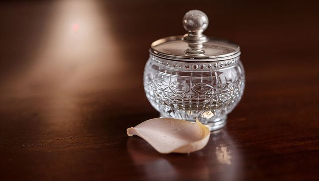 Cut-glass crystal jar with silver lid on polished wood, pale pink petal, warm bokeh