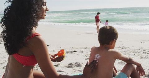 Mother Applying Sunscreen to Son's Back on a Sunny Beach