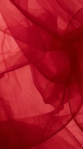 Vertical video showing backlit red voile drifting and folding into translucent layered pleats