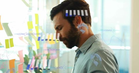 Bearded professional analyzing sticky notes and charts on glass wall for strategic planning