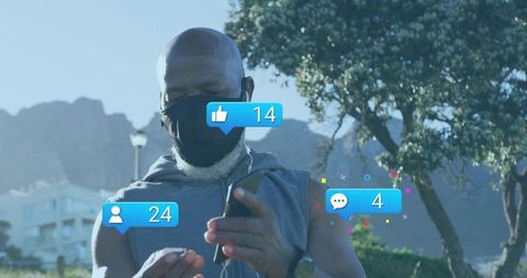 Senior man wearing face mask scrolling smartphone outdoors with social media notifications