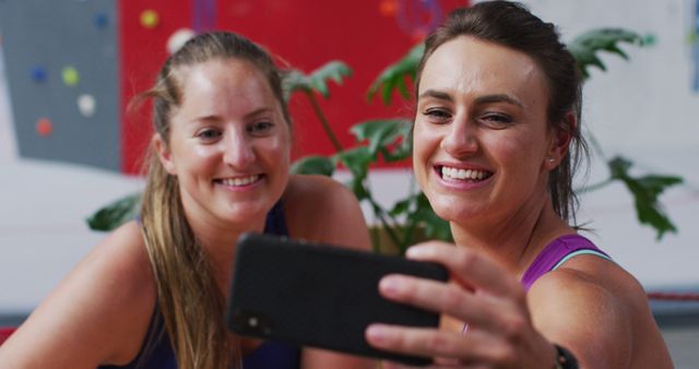Two happy caucasian women taking selfie with smartphone and talking in cafe at indoor climbing wall. fitness and leisure time.