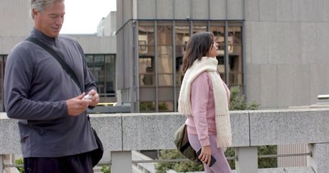 Woman in pink athleisure leaning on city railing while companion using phone
