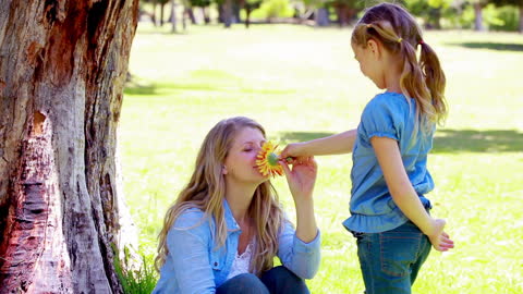 Mother and Daughter Sharing a Flower in a Park