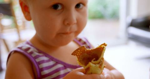Caucasian Child Eating Pancake with Attentive Expression Indoors
