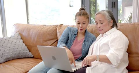 Young woman teaching elderly woman laptop skills on couch