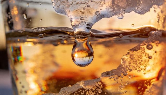 Melting ice droplet hanging in tumbler with amber liquid and warm backlight