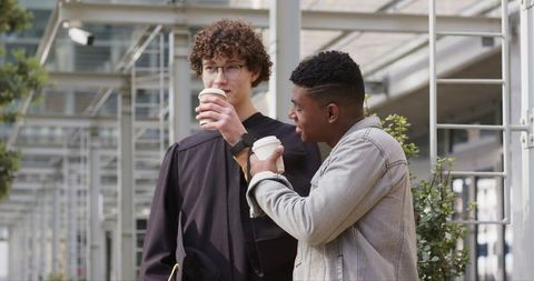 Graduating student and friend sharing coffee under campus pergola celebrating milestone