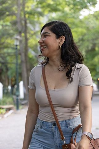 Smiling woman walking in park wearing scoop-neck top, high-waist jeans and crossbody bag