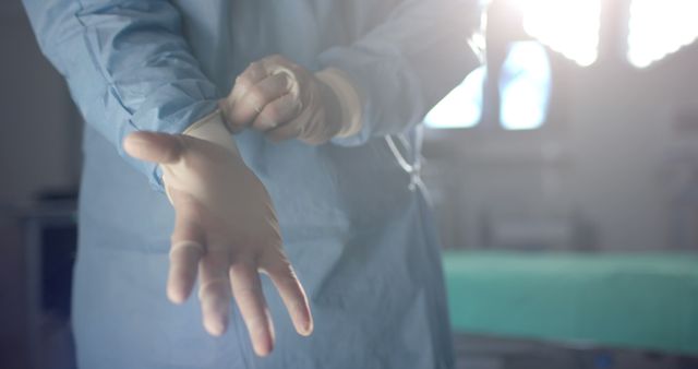 Surgeon putting on gloves in a well-lit operating room, ready to perform a procedure. Sunlight streaming in highlights the preparation process, emphasizing cleanliness and readiness. Ideal for use in medical articles, healthcare websites, or educational materials about surgery and patient care.