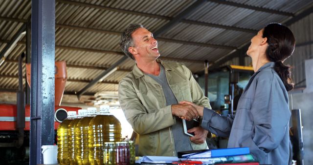 Farmers shaking hands in an olive oil production facility, showcasing successful business cooperation. Suitable for illustrating teamwork, agricultural business deals, and industrial production processes. Ideal for articles, promotional material, and websites highlighting agricultural industry partnerships and agreements.