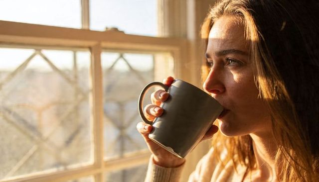 Sipping Morning Coffee by Sunlit Window Woman Holding Gray Mug in Cozy Knit Sweater