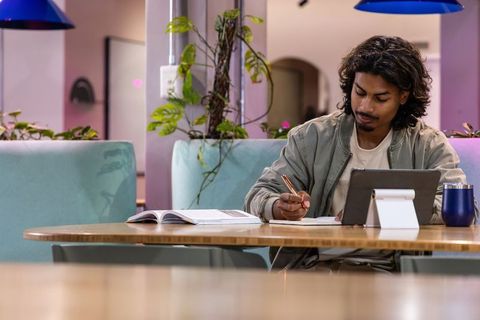 Indian man studying in modern coworking lounge with tablet and notebook
