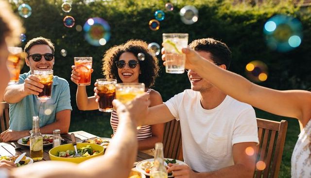 Friends toasting in sunlit backyard with bubbles, summer drinks and outdoor dining