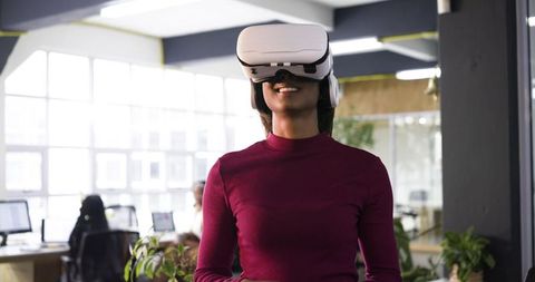 Indian woman wearing white VR headset and headphones smiling in modern office workspace