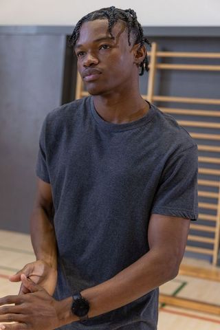 Young african american athlete standing in gym in dark grey tee and watch, focused