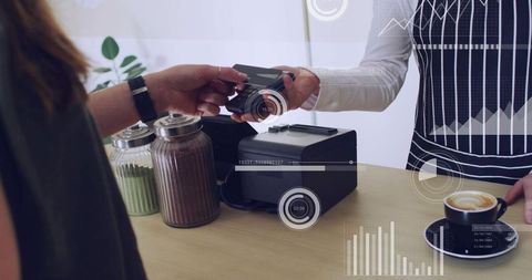 Customer handing card to barista at counter using contactless reader, latte on saucer