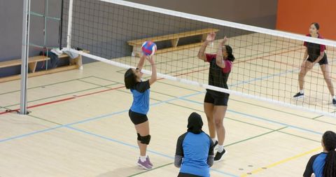 Diverse female volleyball players competing at net in gym passing and blocking during rally