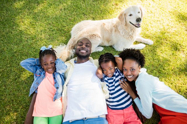 Family enjoying a sunny day outdoors, lying on grass with their dog. Perfect for themes related to family bonding, outdoor activities, pet companionship, and summer leisure. Ideal for use in advertisements, family-oriented content, and lifestyle blogs.