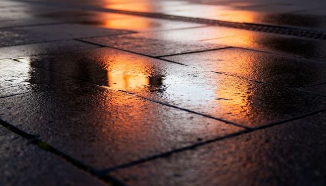Wet stone pavement reflecting warm orange lights at dusk