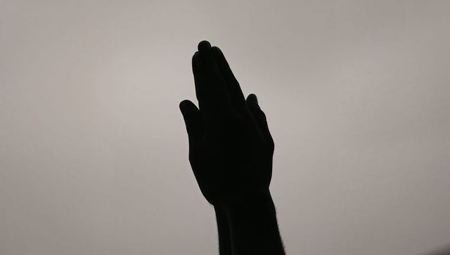 Praying hands silhouette against soft gray gradient minimalist vertical composition