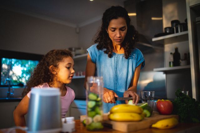 Biracial mother and daughter preparing fruits for smoothie in kitchen. family spending time together at home.