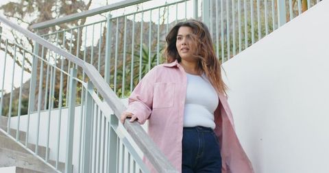 Plus size woman walking up outdoor stairs wearing pink overshirt and high waisted jeans