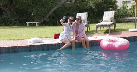 Two women taking selfie at backyard pool on sunny summer day with inflatable donut