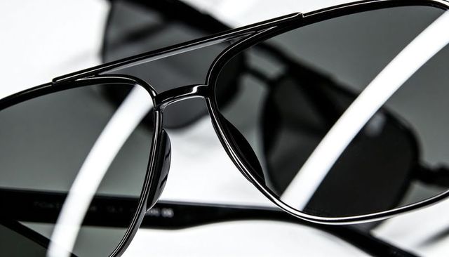 Glossy black aviator sunglasses closeup highlighting metal bridge, nose pads and reflections