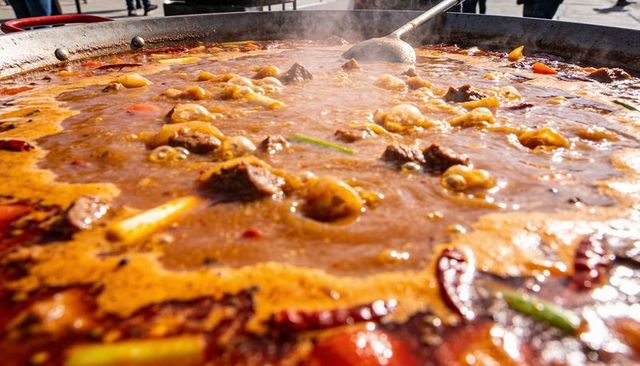 Street market giant pan simmering spicy braised stew with chilies, dumplings, meat, ladle