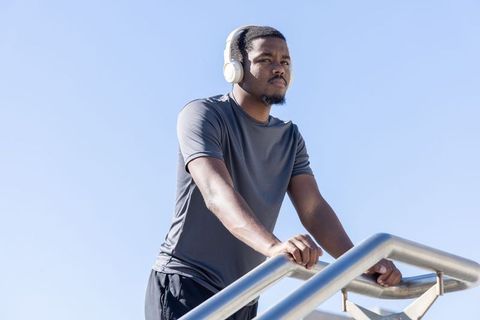 African american man leaning on stair rail listening with white headphones outdoors