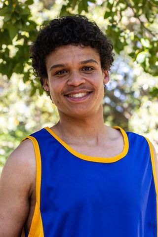African american athlete smiling in blue and yellow jersey under sunlit tree canopy