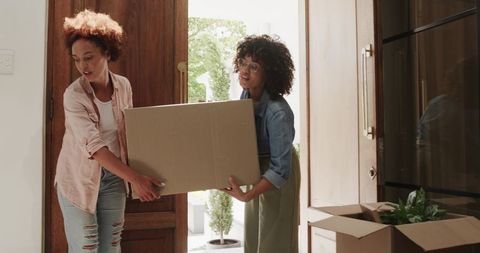 African American Women Carrying Moving Box through Bright Home Entryway, Teamwork Moment