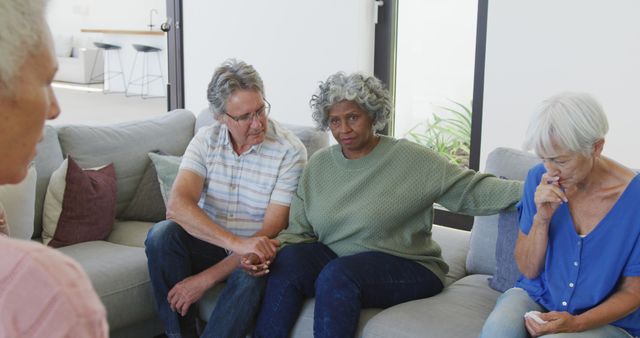 Elderly individuals sitting together on couch, participating in support group therapy, sharing emotions. Scene suggests emotional bonding and open discussion amongst senior citizens. Useful for illustrating elderly mental health support, group therapy sessions, compassion and emotional well-being of older adults.