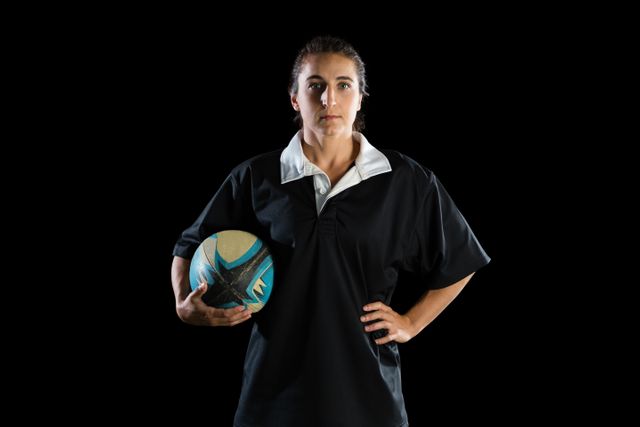 Portrait of female athlete with rugby ball standing against black background