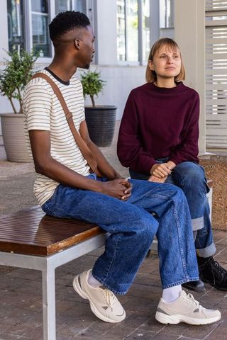 Young friends sitting and talking on bench in urban courtyard with planters, casual chat