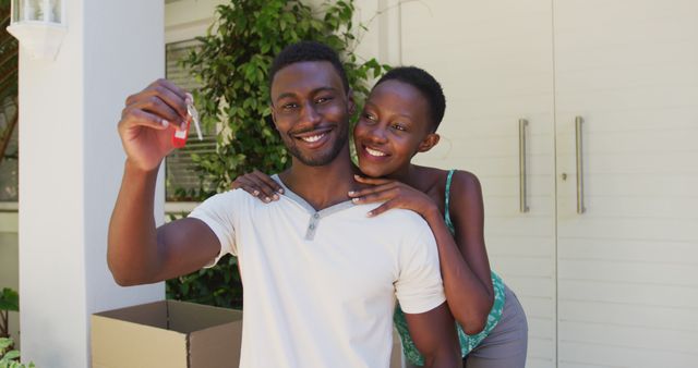 Portrait of smiling african american couple holding house keys and embracing outside their home. staying at home in isolation during quarantine lockdown.