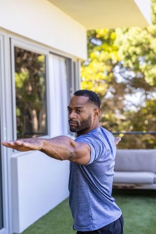 Mature african man stretching arms on sunny balcony for outdoor fitness and wellness