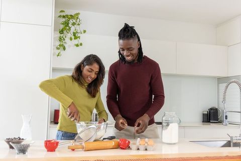 Indian woman and african american man baking together in bright modern kitchen