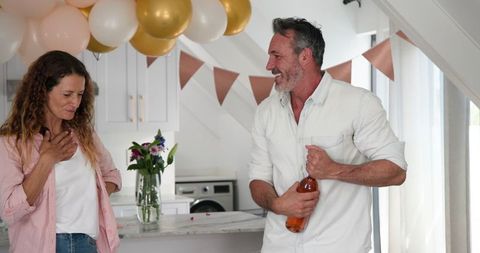 Joyful couple surprise celebration in kitchen with balloons