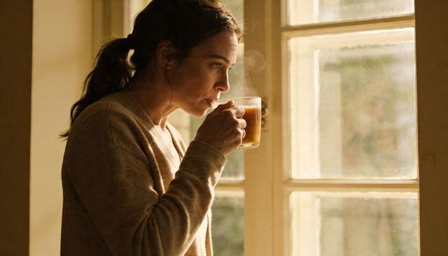 Woman sipping steaming coffee while gazing out sunlit window, quiet morning mood