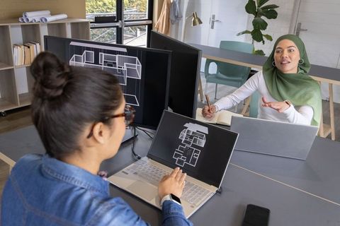 Diverse female architects collaborating on digital floorplans in modern coworking office
