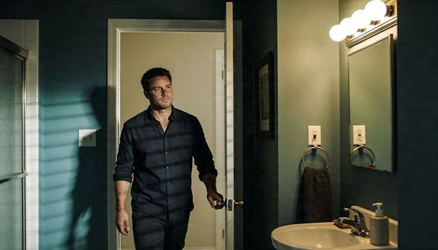 Man walking into bathroom holding doorknob looking thoughtful under vanity light