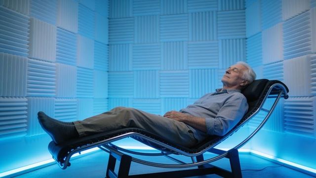 Senior man reclining on modern chaise in acoustic foam room with blue ambient lighting
