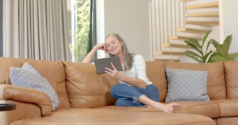 Mature woman relaxing on sofa with tablet at home