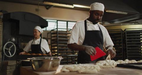 Artisan bakers shaping braided loaves in industrial bakery kitchen using dough scraper