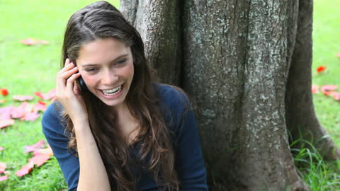Young Woman Laughing on Phone Under Tree
