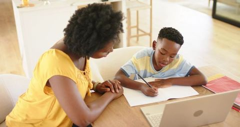 African American mother helping son with homework at kitchen table during remote learning