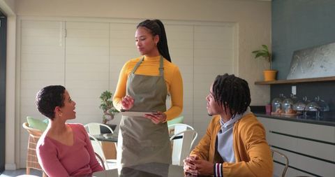 Young Server Taking Order on Tablet Serving Diverse Customers in Sunlit Modern Cafe